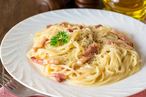 Classic pasta carbonara. Spaghetti with bacon, egg yolk and parmesan cheese on white plate on dark wooden background.