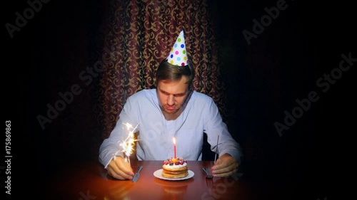 a lone man celebrates a holiday, he sits alone at a table with a cake and a candle. 4k, slow motion photo