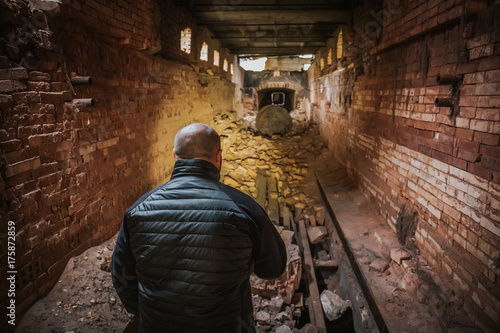 Man with flashlight in dark underground brick tunnel or corridor of abandoned brick factory, view from back, perspective