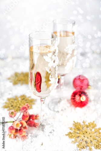 Two champagne glasses on light bokeh background. New Year and Christmas Celebration. Red baubles, berries, garland, tree ornaments and gift boxes