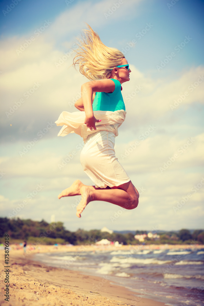 Blonde woman wearing dress playing jumping on beach Blonde woman wearing dress playing jumping on beach