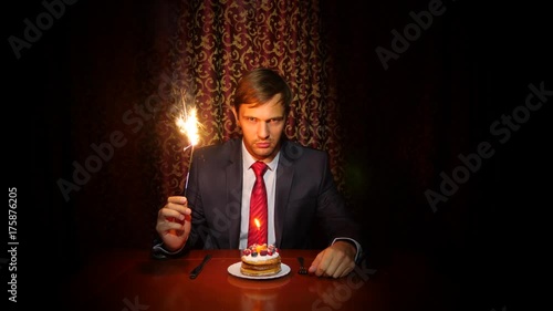 a lone man celebrates a holiday, he sits alone at a table with a cake and a candle. 4k, slow motion photo