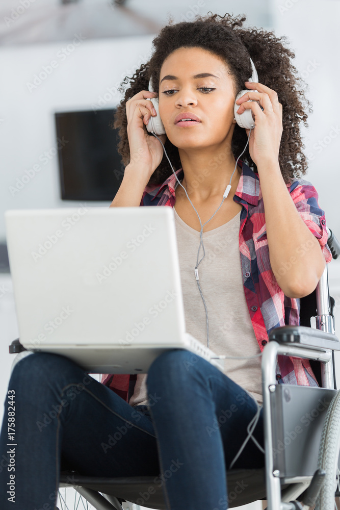 Young lady in wheelchair with laptop and headphones Young lady in wheelchair with laptop and headphones