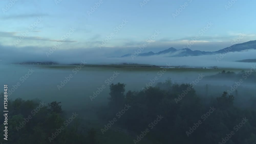 AERIAL Thick fog spreading across the vast valley underneath high rocky mountains on early winter morning. Spooky misty scenery. Agricultural countryside with vast meadow fields enveloped in heavy fog AERIAL Thick fog spreading across the vast valley underneath high rocky mountains on early winter morning. Spooky misty scenery. Agricultural countryside with vast meadow fields enveloped in heavy fog