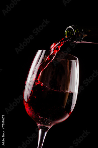 Red wine pouring in wineglass from a bottle on black background. Wine list design menu with copyspace.