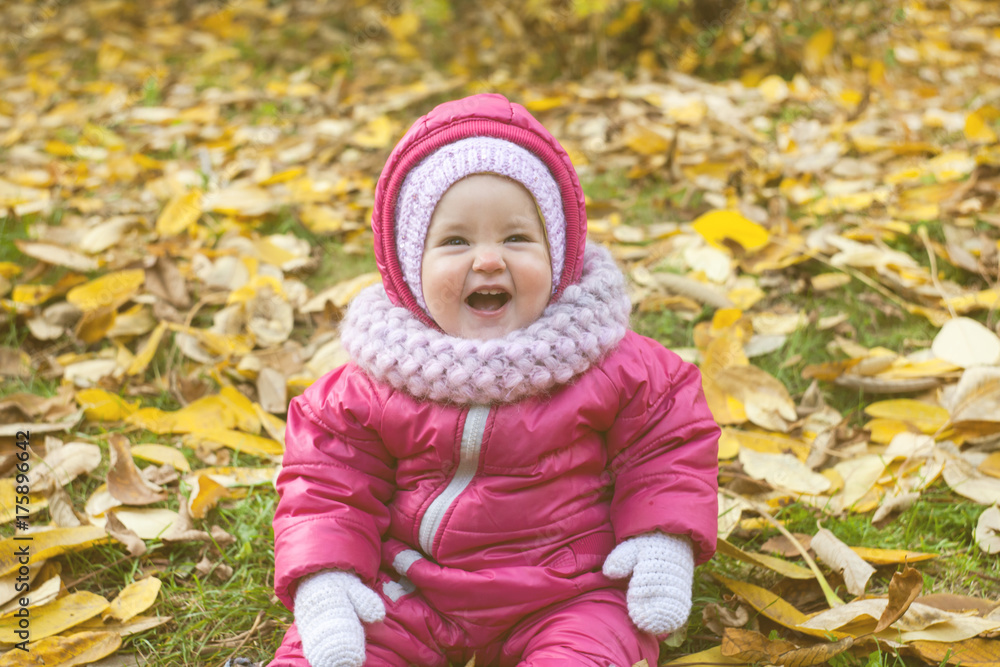 Portrait of happy little baby girl playing with yellow autumn leafs at natural outdoors park background