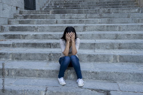 beautiful and sad Hispanic woman desperate and depressed sitting on urban city street staircase