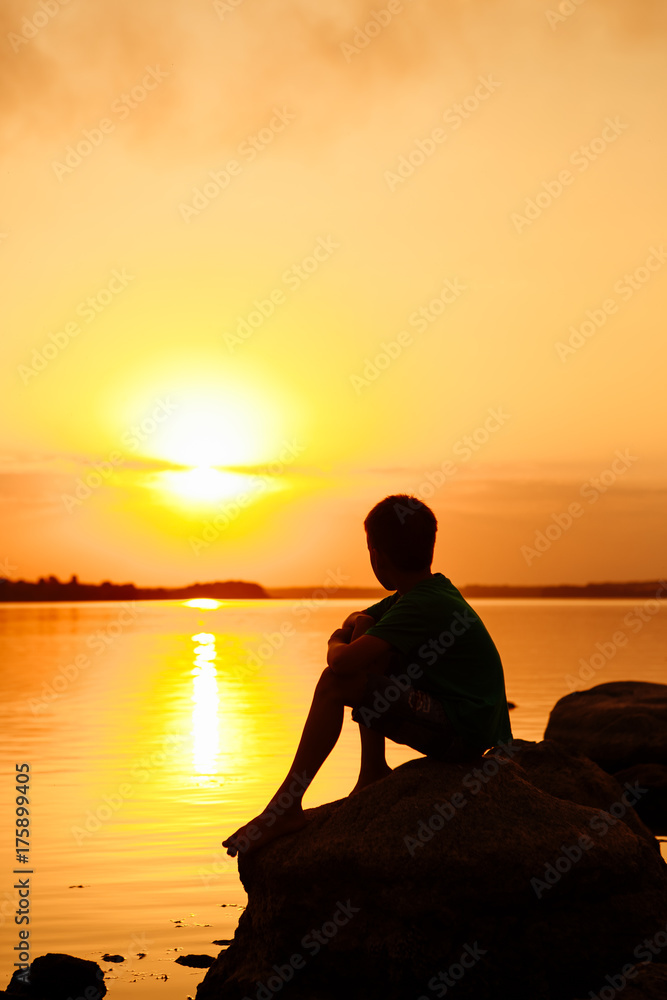 A little boy is watching the sunset against the background of a river. Dreams Come True.