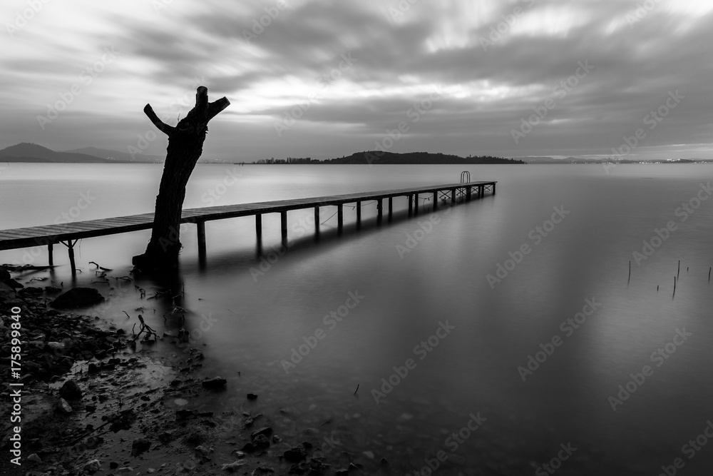 Fototapeta premium Long exposure view of a pier on a lake, with moving clouds and perfectly still water