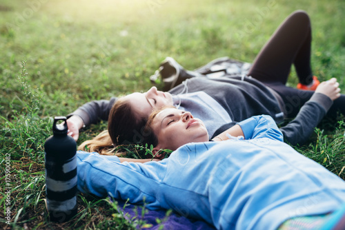 Fotografie Two young sportswomen laying on grass with eyes closed relaxing after outdoor wo