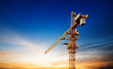 Industrial construction cranes and building silhouettes over sun at sunrise.