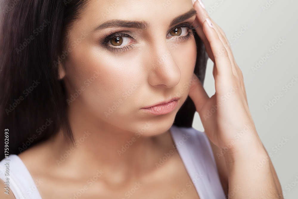 A tired, exhausted young woman who suffers from a severe headache of tension. Sufferers from headache. Migraines A sense of pressure and stress. On a gray background. A tired, exhausted young woman who suffers from a severe headache of tension. Sufferers from headache. Migraines A sense of pressure and stress. On a gray background.