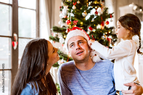 Young family with daughter at Christmas tree at home.