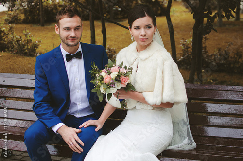 Happy bride and groom are sitting in the park in autumn. Wedding newlyweds