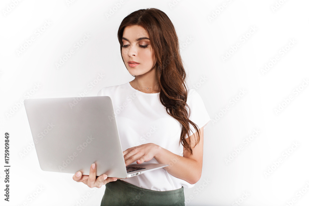 Brunette woman dressed in business style works on the laptop holding it in her arms Brunette woman dressed in business style works on the laptop holding it in her arms