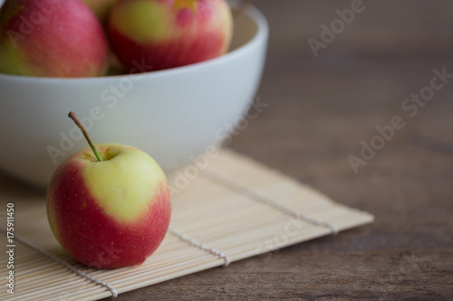 Fuji apple on bamboo mat put on rustic wood table and stack in white bowl with copy space. Delicious sweet and juicy fuji apple suitable for salad cooking or bakery. Fuji apple has origins in Japan.