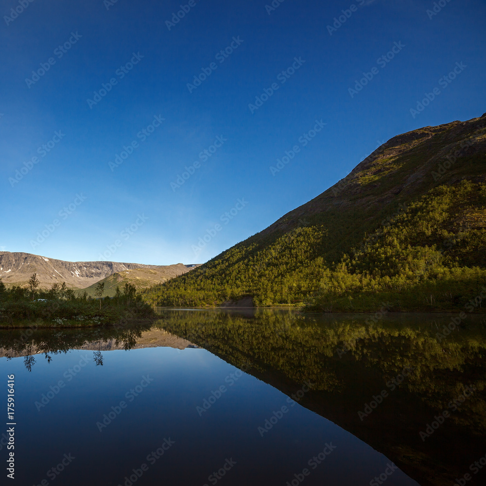 Fototapeta premium Mountains reflected in the smooth surface of the lake at dawn.
