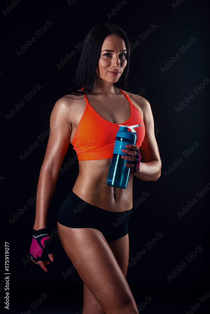Cute athletic girl in sportswear relaxing after workout with shaker  isolated over black background. Healthy young woman drinks whey protein.  Stock Photo