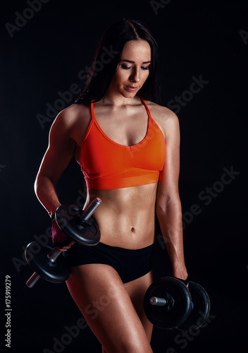 Nice sexy girl doing workout with dumbbells isolated over black background. Athletic young woman do a fitness workout with weights.