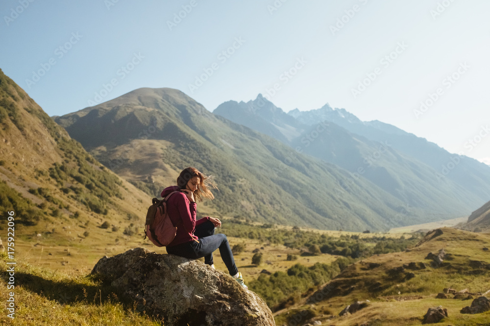 a young woman traveler with backpack enjoying view of autumn mountains, rear view