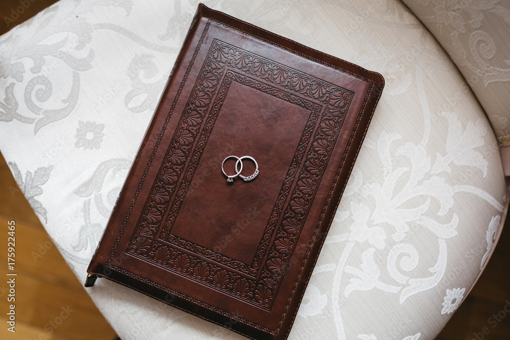 Fototapeta premium Silver wedding rings lie on the book in leather cover
