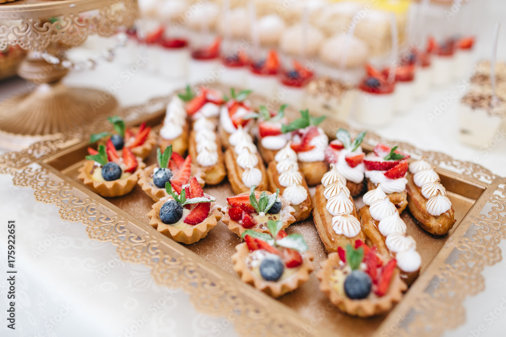 Delicious cookies with strawberries, macaroons and eclairs  served on golden dish