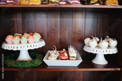 Colorful macaroons served on large white dish on a wooden shelf with other sweets