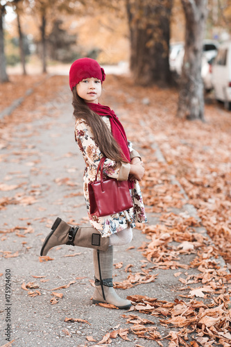 Stylish baby girl 4-5 year old wearing trendy winter jacket walking in park. Looking at camera. Autumn season.
