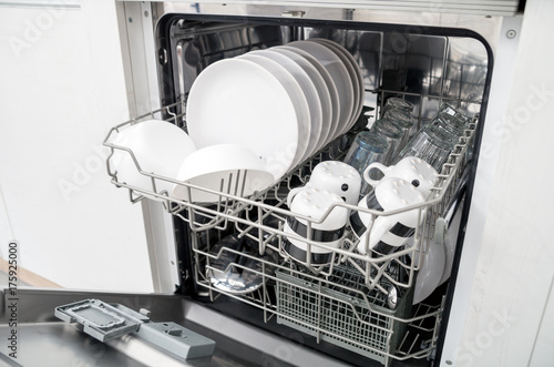 Open dishwasher with clean dishes in white kitchen
