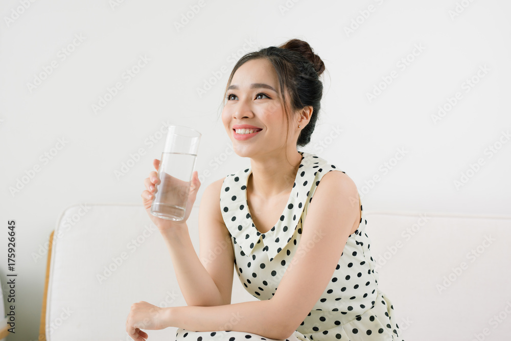Young beautiful asian woman holding a glass of water while sitting at home Young beautiful asian woman holding a glass of water while sitting at home
