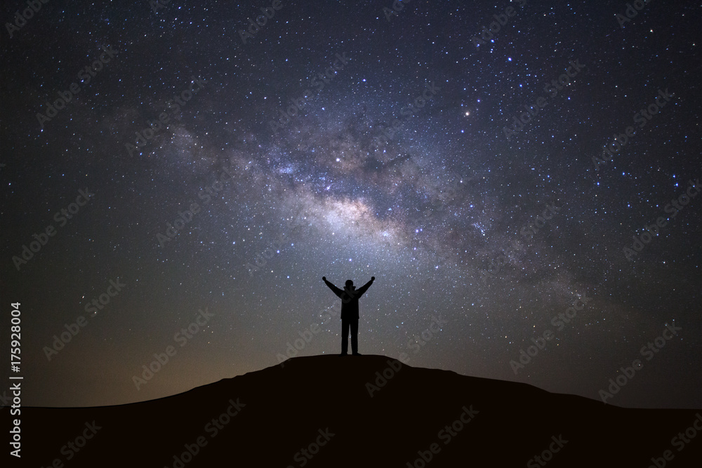Naklejka premium Landscape with milky way galaxy, Starry night sky with stars and silhouette of a standing sporty man with raised up arms on high mountain.