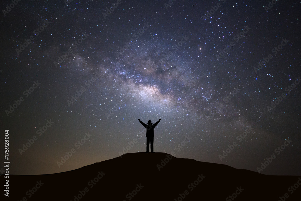 Landscape with milky way galaxy, Starry night sky with stars and silhouette of a standing sporty man with raised up arms on high mountain.