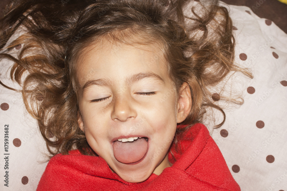 A truly beautiful little girl with shaggy hair on the pillow in red plaid