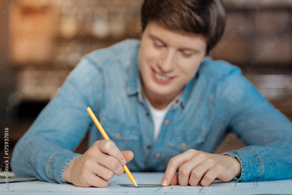 Smiling man using a protractor while drawing blueprint Smiling man using a protractor while drawing blueprint