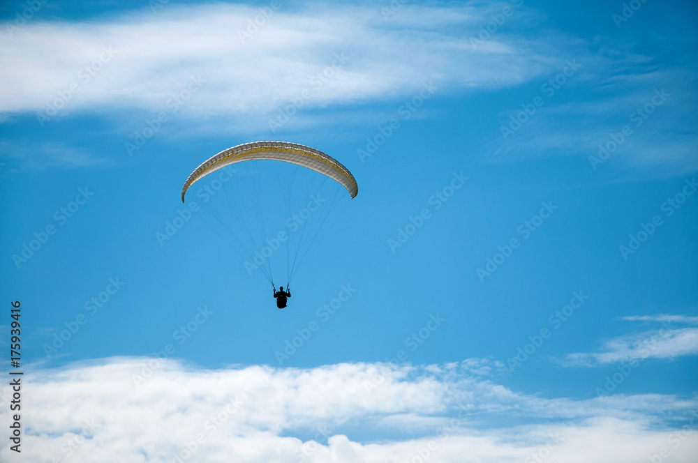 Paraglider flying in the blue sky against the background of clouds. Paragliding in the sky on a sunny day. Paraglider flying in the blue sky against the background of clouds. Paragliding in the sky on a sunny day.