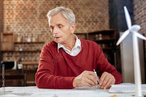 Grey-haired man using compass to draw blueprint