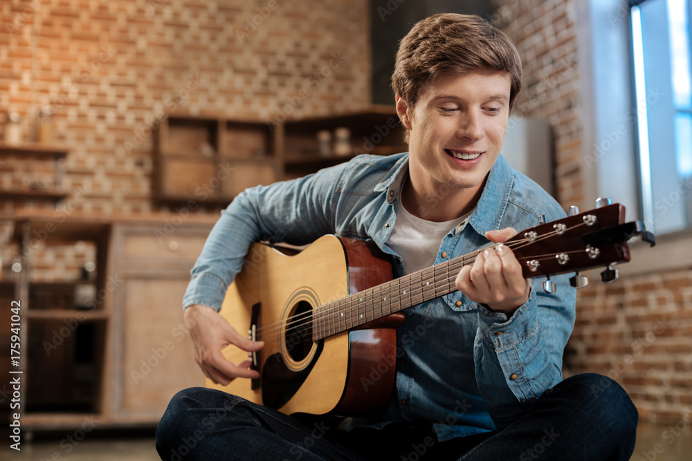 Obraz premium Cheerful young man playing guitar and smiling