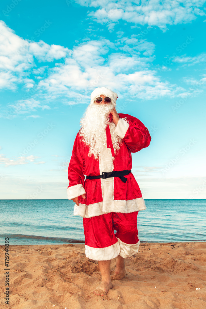 Obraz premium Santa Claus with a bag of gifts on the beach. The symbol of Christmas.