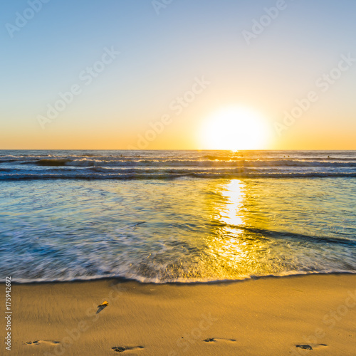 Fototapeta Naklejka Na Ścianę i Meble -  The bright sun of California. Footprints on the sand of the beach. Sunset bright sun sets over the horizon. Beautiful beaches of California. South of the USA
