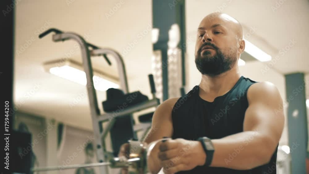 White bald bearded man on rowing machine in gym, orange teal look grade White bald bearded man on rowing machine in gym, orange teal look grade