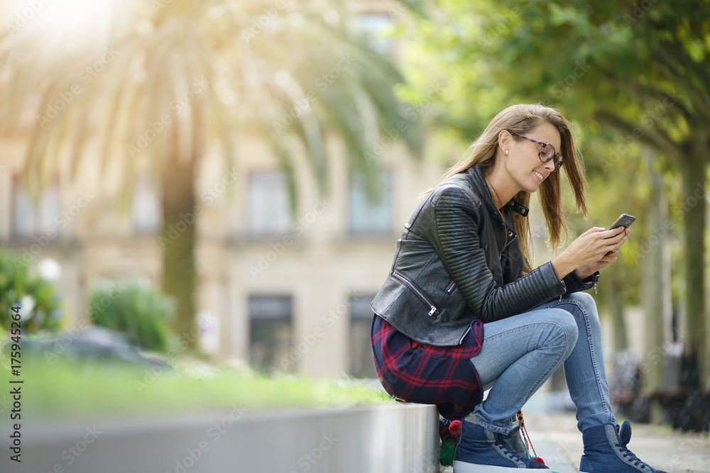 Young woman sitting in park, using smartphone