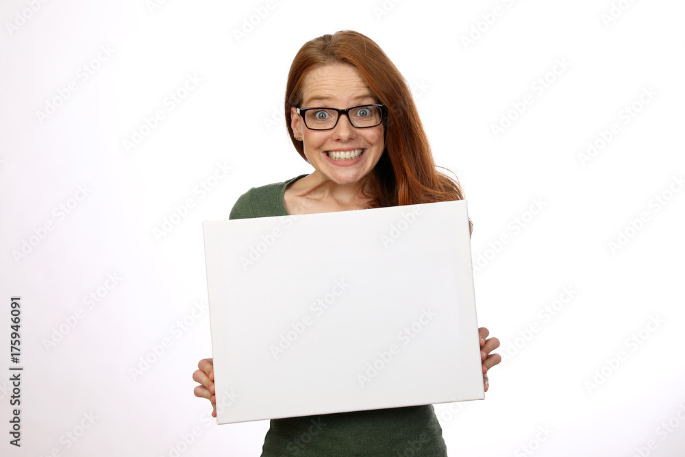 Hübsche rothaarige Frau mit Brille hält weisse Tafel in den Händen begeistert