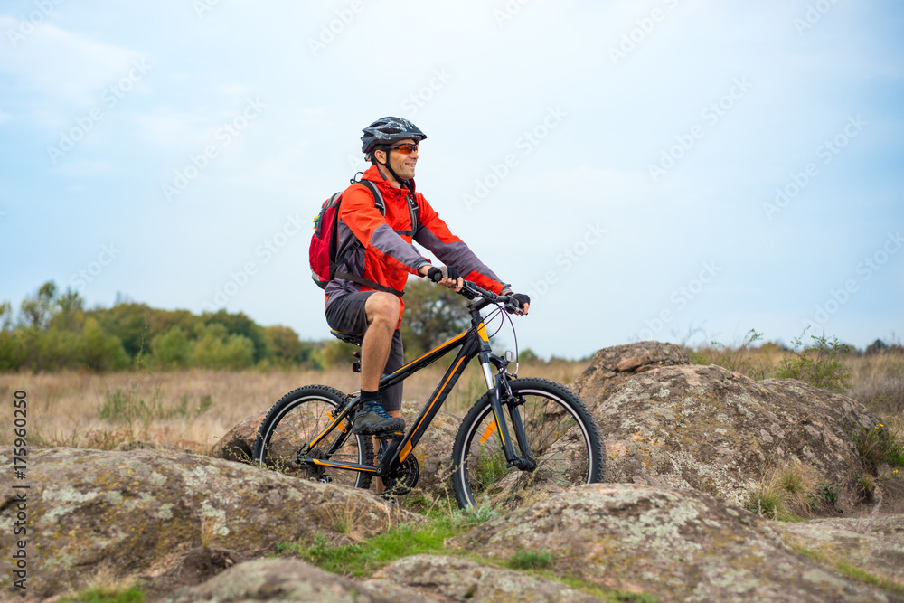 Happy Cyclist in Red Resting on the Bike on Rocky Trail. Adventure Sport and Travel Biking Concept.