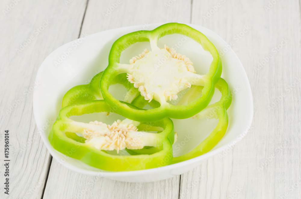 Heap of slices of green fresh ripe raw pepper in ceramic bowl on old rural white wooden planks Heap of slices of green fresh ripe raw pepper in ceramic bowl on old rural white wooden planks