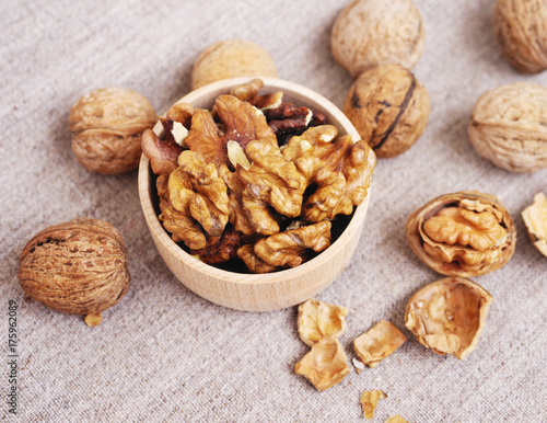 Walnut kernels in a wooden bowl and whole walnuts on a table. Walnuts