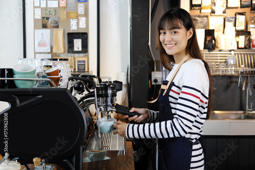 Smiling asian barista preparing cappuccino with coffee machine. Cafe restaurant service, Small business owner, food and drink industry concept.