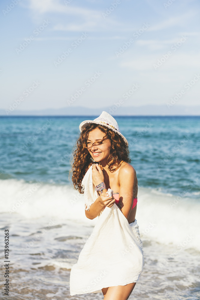 Attractive woman with white scarf and hat, enjoying the water and the sunlight on the beach Attractive woman with white scarf and hat, enjoying the water and the sunlight on the beach