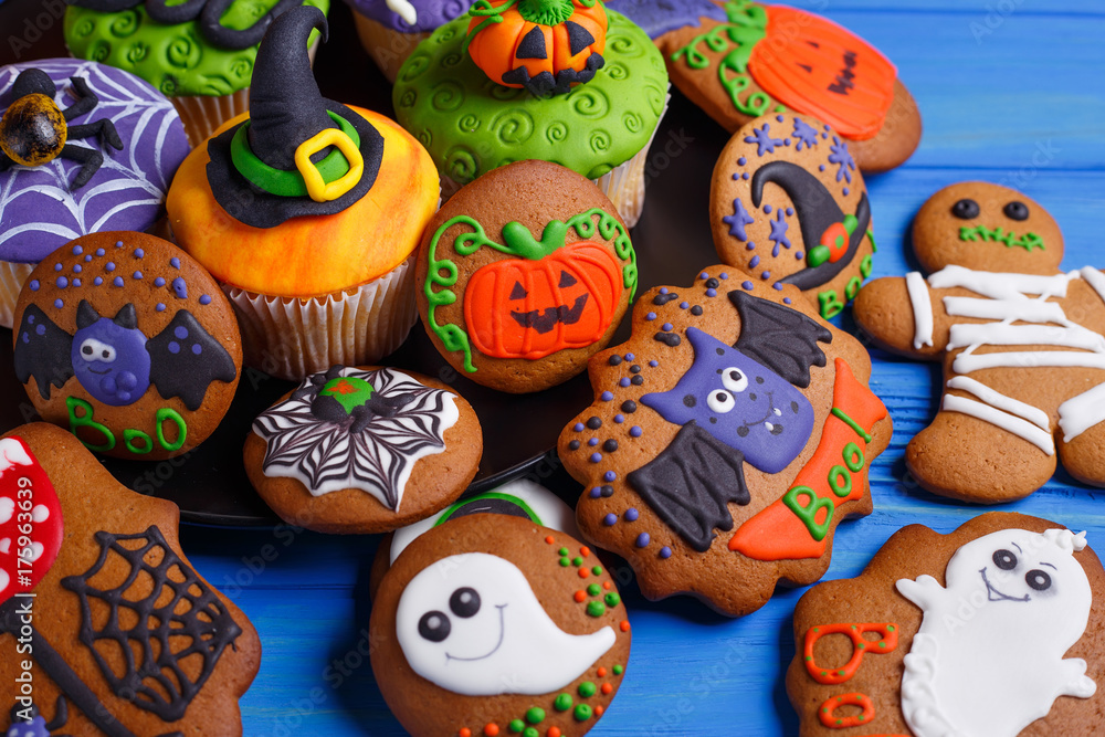 Halloween dessert: funny monsters, ghosts and pumpkins made of biscuits with confectionery mastic decorations on the table, close-up