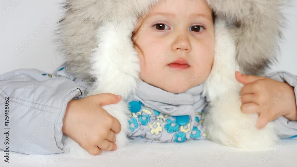 A funny child dressed in warm fur clothes and looking at the camera. Close-up portrait. The concept of winter, frost and snow, cold weather, cool temperature and Christmas. A funny child dressed in warm fur clothes and looking at the camera. Close-up portrait. The concept of winter, frost and snow, cold weather, cool temperature and Christmas.
