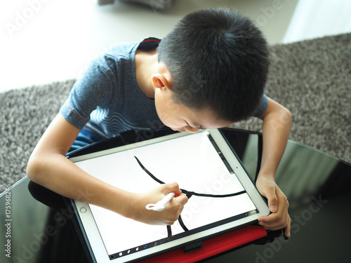 Asian boy doing digital drawing on tablet.